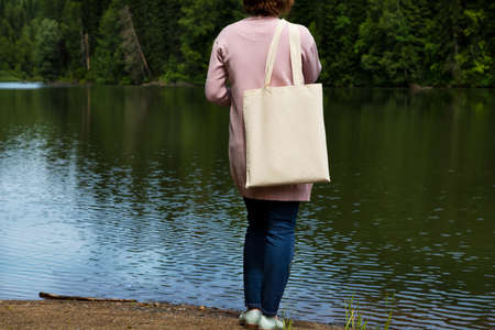Woman in pink jacket carrying shopping bag mockup. Female hand holding canvas eco friendly tote bag mock upの写真素材