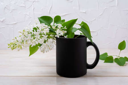 Black coffee mug mockup with tender blooming white lilac branch. Empty mug mock up for brand promotionの写真素材
