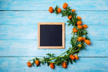 Black chalkboard wooden square frame mockup with globeflowers on the blue table. Empty blackboard frame mockup for presentation design. Template black felt letter board framing for modern art.の写真素材
