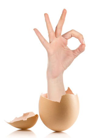 Hand with broken egg isolated on white backround.Female hand showing thumb up ok all right victory hand sign gesture. Gestures and signs. Body language on white backgroundの写真素材