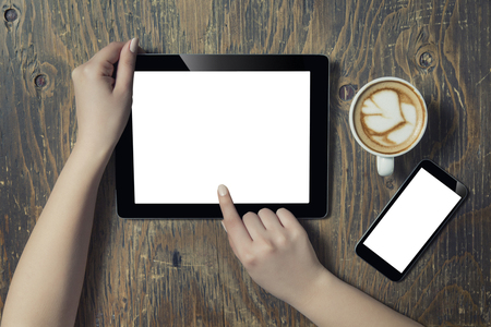 Businesswoman reading his tablet with white screen and a cup of coffee smartphone in coffee cafe. Woman hands holding tablet pc with empty screen on wooden backgroundの写真素材