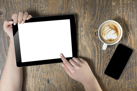 Businesswoman reading his tablet with white screen and a cup of coffee smartphone in coffee cafe. Woman hands holding tablet pc with empty screen on wooden backgroundの写真素材