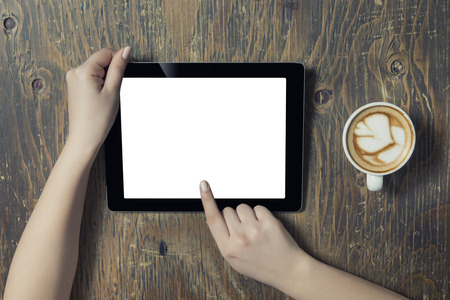 Businesswoman reading his tablet with white screen and a cup of coffee smartphone in coffee cafe. Woman hands holding tablet pc with empty screen on wooden backgroundの写真素材