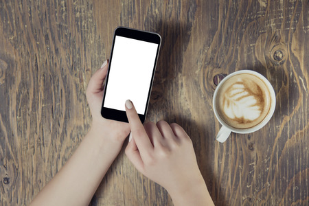 Businesswoman reading his tablet with white screen and a cup of coffee smartphone in coffee cafe. Woman hands holding tablet pc with empty screen on wooden backgroundの写真素材