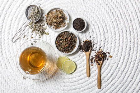 Food background with different black and green dry tea, rose buds cup of hot tea and iron teapot over dark wooden background. Tea drinking concept. Top view. Square imageの写真素材