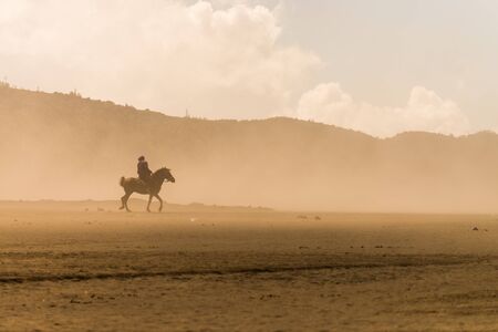 horse rider riding on desert in sand stormの写真素材