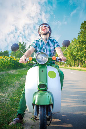 A cheerful guy cheerfully laughs very quickly rides a retro scooterの写真素材