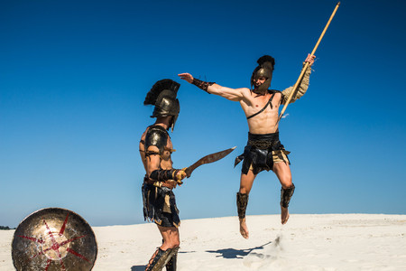 An ancient warrior with a spear in a jump attacks a Spartan with a sword