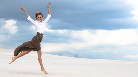 Cheerful girl jumping in the desert against the skyの写真素材