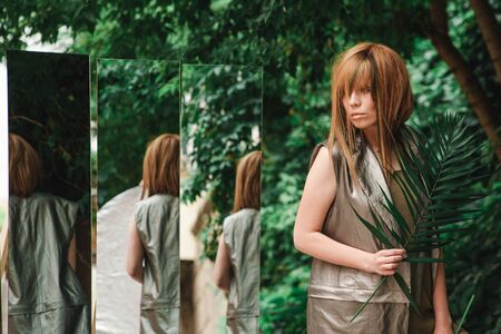 A girl with a palm branch in her hand looks carefully into the mirrorの写真素材