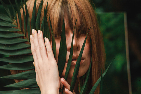 A girl with a golden manicure, make-up and hair is holding a fern branchの写真素材