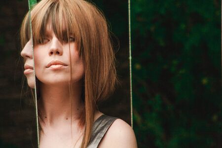 A girl stands between the mirrors in the forest and looks at her reflectionの写真素材