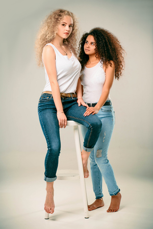 Blonde and African American are sitting on a chair in jeans and white T-shirtsの写真素材