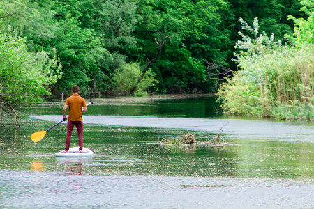 View from the back of a man on a sup board swims along the river