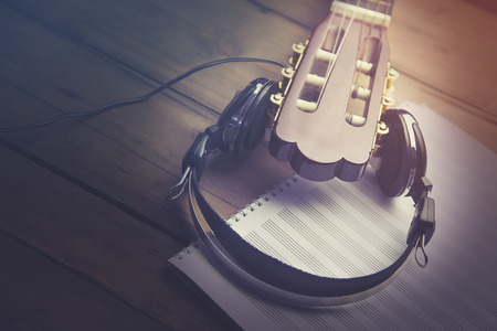 white earphone on the guitar and notepad on wooden table