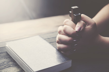 Hands of Christian woman praying on wooden desk