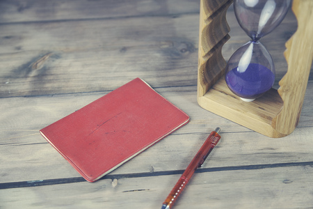 notebook, pen, and hourglass on wooden tableの写真素材