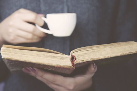 Young woman reading a book and holding cup of coffee