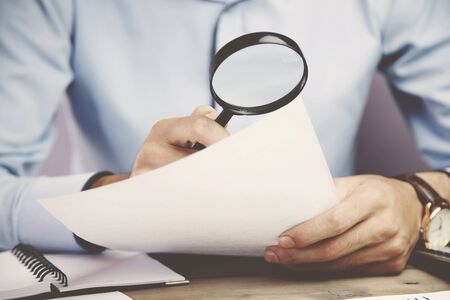 Businessman looking through a magnifying glass to documentsの写真素材