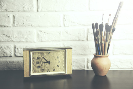 clock and brushes on table  on brick wall background