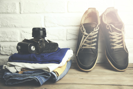 man sneakers and camera on clothing on wooden table on brick wall backgroundの写真素材