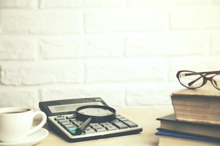 glasses on books and magnifying glass on calculator, coffee on table on brick wall bacgroundの写真素材