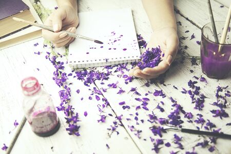 woman hand brush on notebook,flower petals, watercolor on tableの写真素材