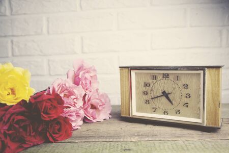 colorful roses and  clock on wooden table on brick wall backgroundの写真素材