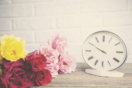 colorful roses and  clock on wooden table on brick wall backgroundの写真素材
