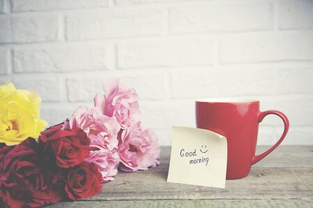 Coffee cup with rses and notes good morning on wooden table on brick wall backgroundの写真素材