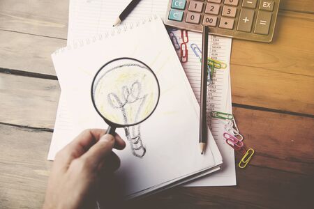 man hand magnifying glass and bulb on notebookの写真素材