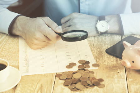 man hand magnifierand  phone,money and coffee on wooden tableの写真素材