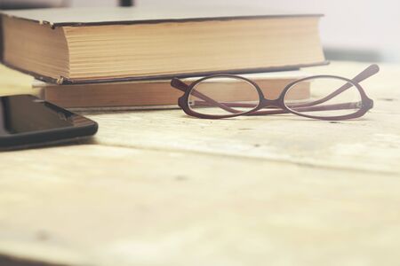 Old vintage books, smartphone and glasses on a wooden tableの写真素材