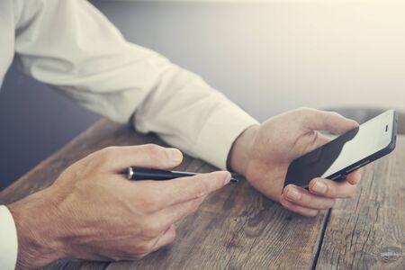hand holding smartphone and pen on wooden background