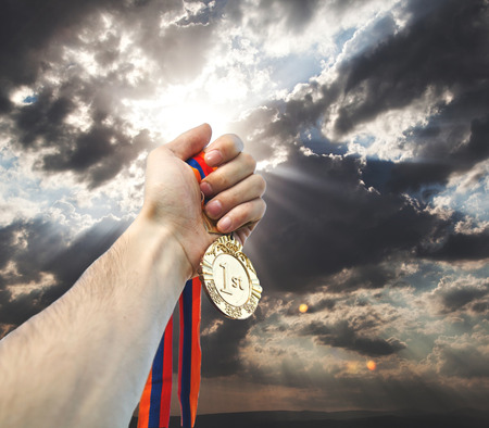 Golden medal in man  hand on sky backgroundの写真素材