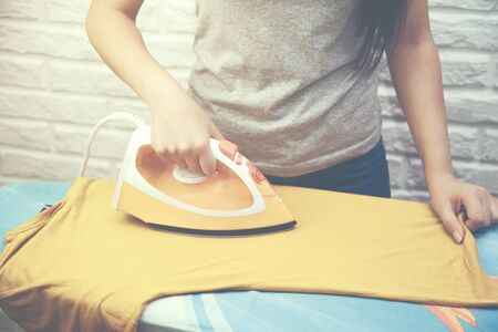 Young woman ironing yellow T-shirtの写真素材
