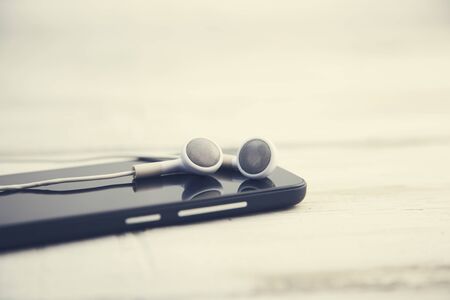 Smartphone and earphones on table. Focus on earphones.の写真素材