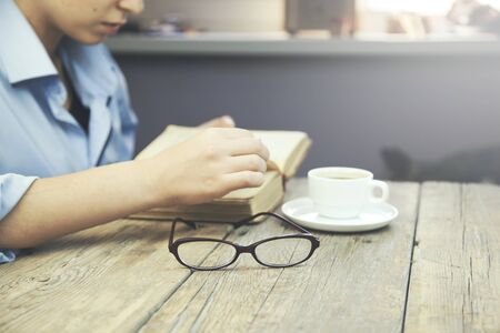 woman sitting by wooden table and reading bookの写真素材
