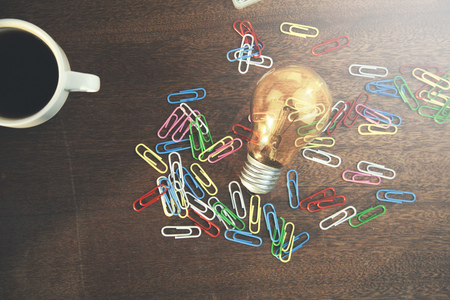 Flat lay, a lots of colorful paper clips,bulb and coffee on wooden tableの写真素材