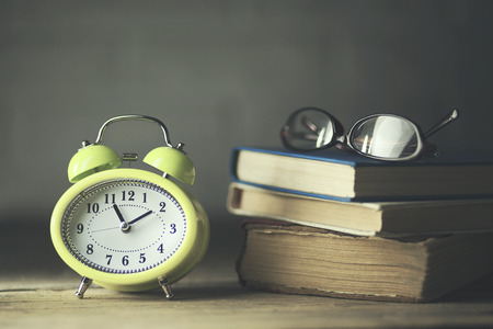 analog retro alarm clock,books and glasses on wooden table