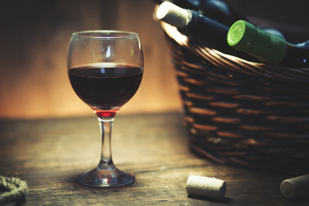 Wine bottles in basket and glass on wooden tableの写真素材