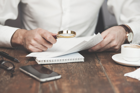 Businessman looking through a magnifying glass to documentsの写真素材