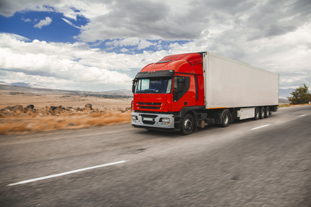 Red truck on blurry asphalt road over blue cloudy sky backgroundの写真素材