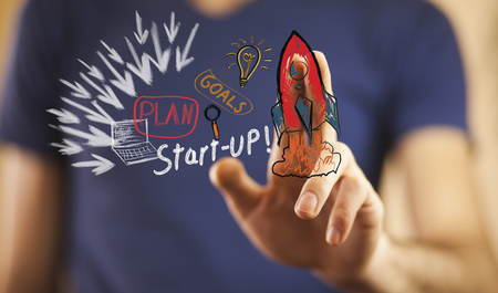 Businessman on blurred background holding hand drawn startup text and red rocket in his handの写真素材