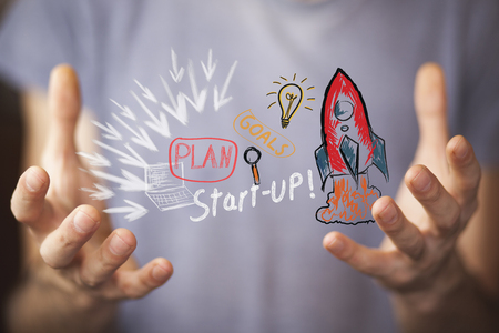 Businessman on blurred background holding hand drawn startup text and red rocket in his handの写真素材