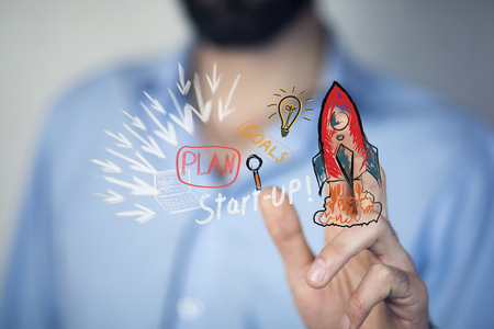 Businessman on blurred background holding hand drawn startup text and red rocketの写真素材