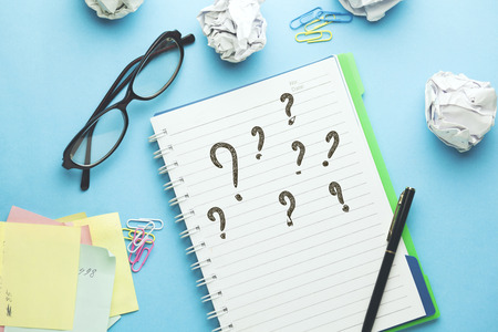 Question Mark written on a white notebook with  glasses on blue backgroundの写真素材