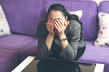 young woman sitting in sofa hand eyesの写真素材
