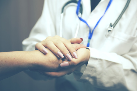 woman doctor's hands holding female patient's hand for encouragement and empathyの写真素材