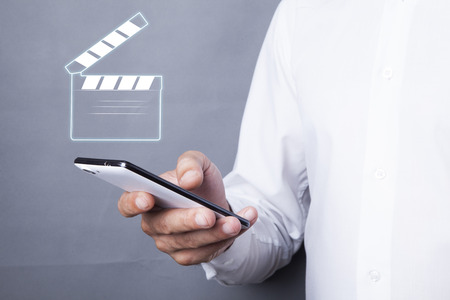 man hand holding a phone with movie clapper in screenの写真素材